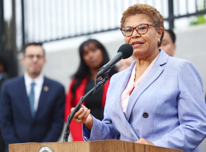 A Black woman in a lavender suit speaks into a microphone.