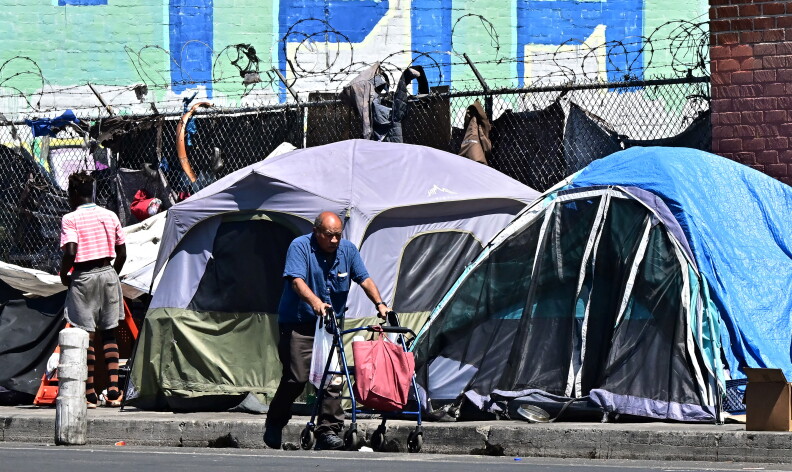 A man pushes a cart in front of tents on a sidewalk.