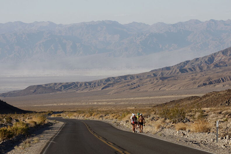 Four people walking along the side of a two-lane road in a dry, hot desert