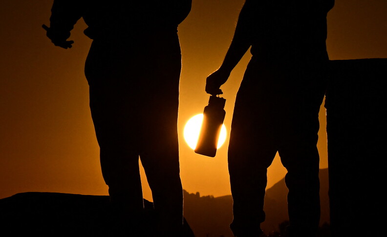A man holds a water bottle while hiking at sunset in Los Angeles.