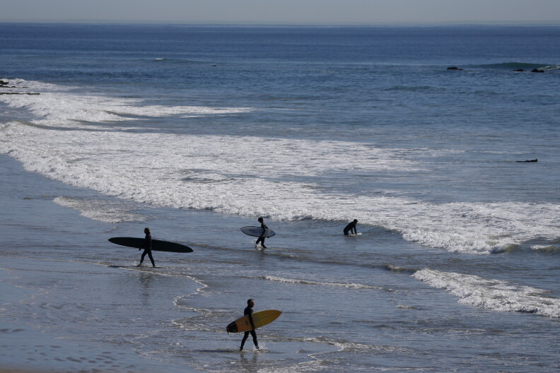 Four people with surfboards head to the ocean.