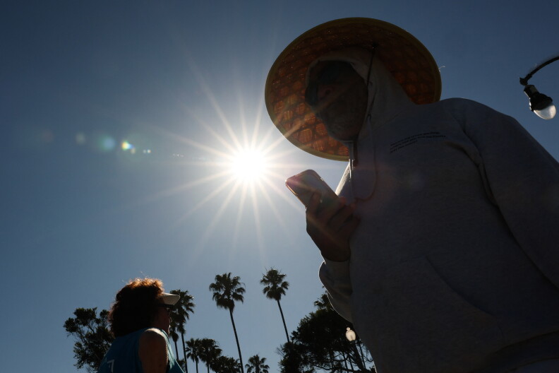 The sun shines brightly on a person wearing a hat and holding a phone.