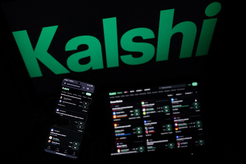 A phone screen and a laptop screen are lit with small icons. The words "Kalshi" are glowing behind them in a dark room.