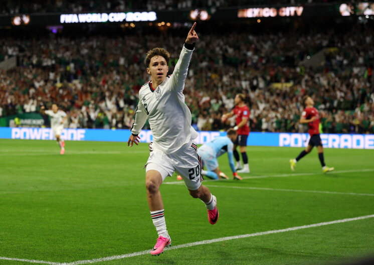 A man in a white uniform points into the air on a soccer pitch.