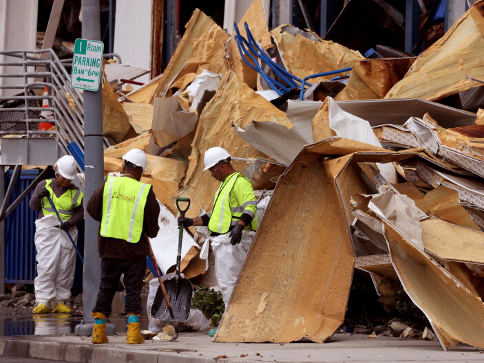 Workers in reflective vests hold tools near a mass of debris.