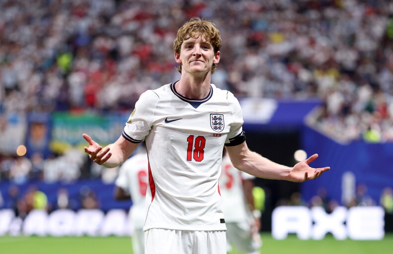 A soccer player wearing a white jersey holds his hands out to the side while shrugging his shoulders.