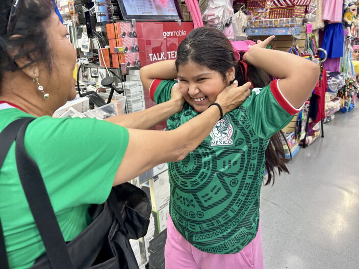 A girl holds her arms up and wears a green sports jersey. Her mother holds her cheeks in a caring way.