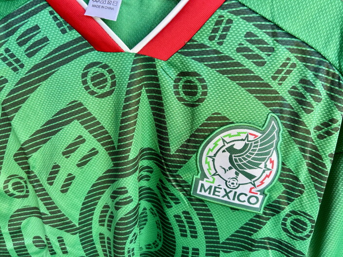 A greeen sports jersey with geometric designs and a logo with an eagle and the word, "Mexico".