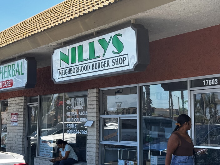 The exterior of Nilly's Neighborhood Burger Shop with a green and white sign above the storefront on a sunny day in Artesia.