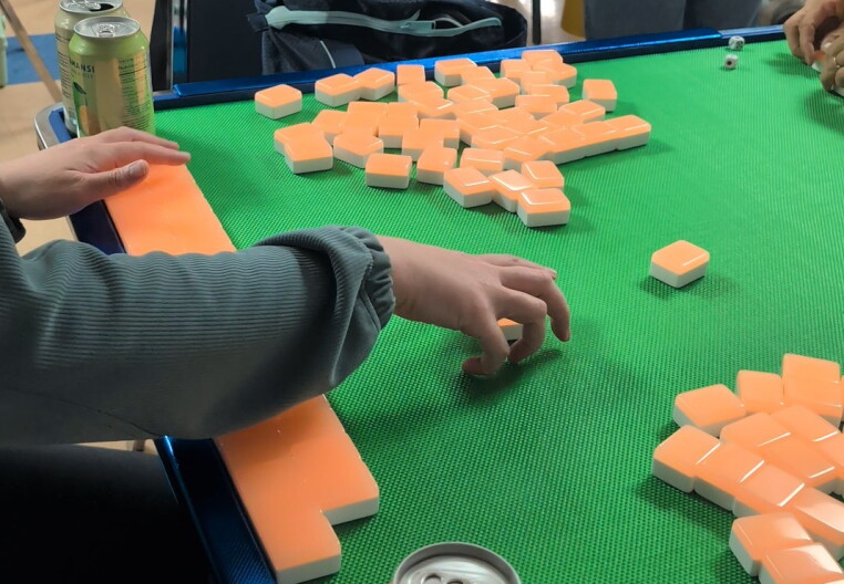 A hand reaching for a Chinese mahjong game tile on top of a table.