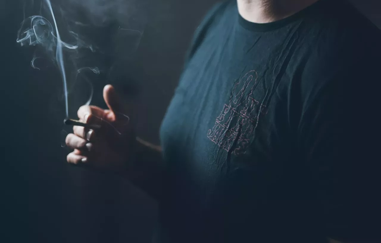 A man holds a burning joint in between puffs