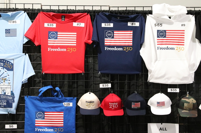 Shirts tied to America’s 250th birthday are sold in a stall at Freedom 250’s Great American State Fair in Washington, D.C., on June 30, 2026. (Photo by Sam Gauntt/States Newsroom)