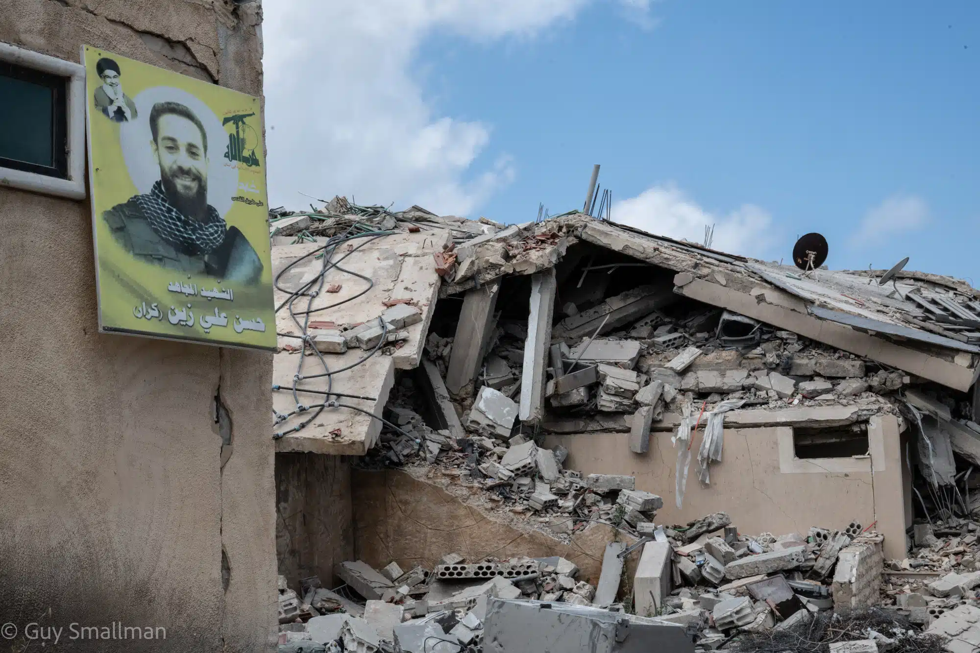 A destroyed building in South Lebanon with a resistance martyr poster in the foreground