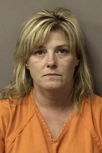 A mug shot of a woman with blonde hair and brown eyes, who is wearing an orange jumpsuit.