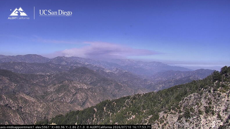 Smoke from a distant fire rises over mountainous terrain.