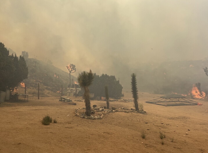 Fire burns in a desert area. The air is thick with smoke. A van is visible.