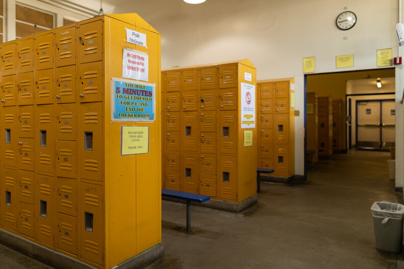 A locker room with three section of yellow lockers in rows and blue benches in the center of each aisle.