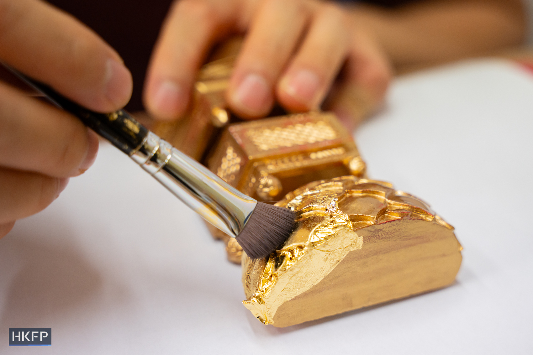 Sylverster Siu demonstrate the process of applying gold leaf on statues. Photo: Kyle Lam/HKFP.