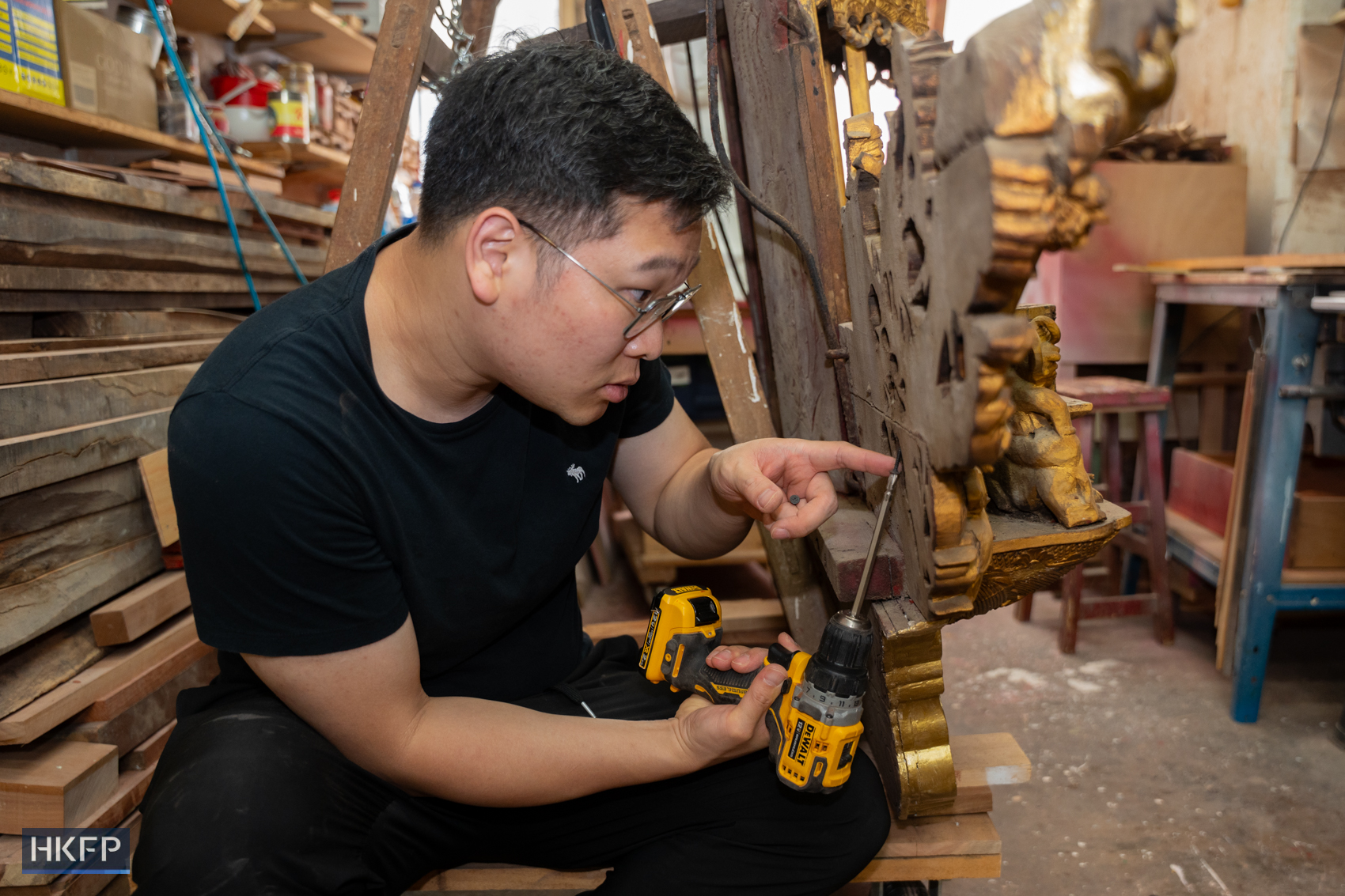 Sylverster Siu use an electric drill to secure the wooden decoration during repairing in an industrial building in Kwai Chung area, June 12th, 2026. Photo: Kyle Lam/HKFP.