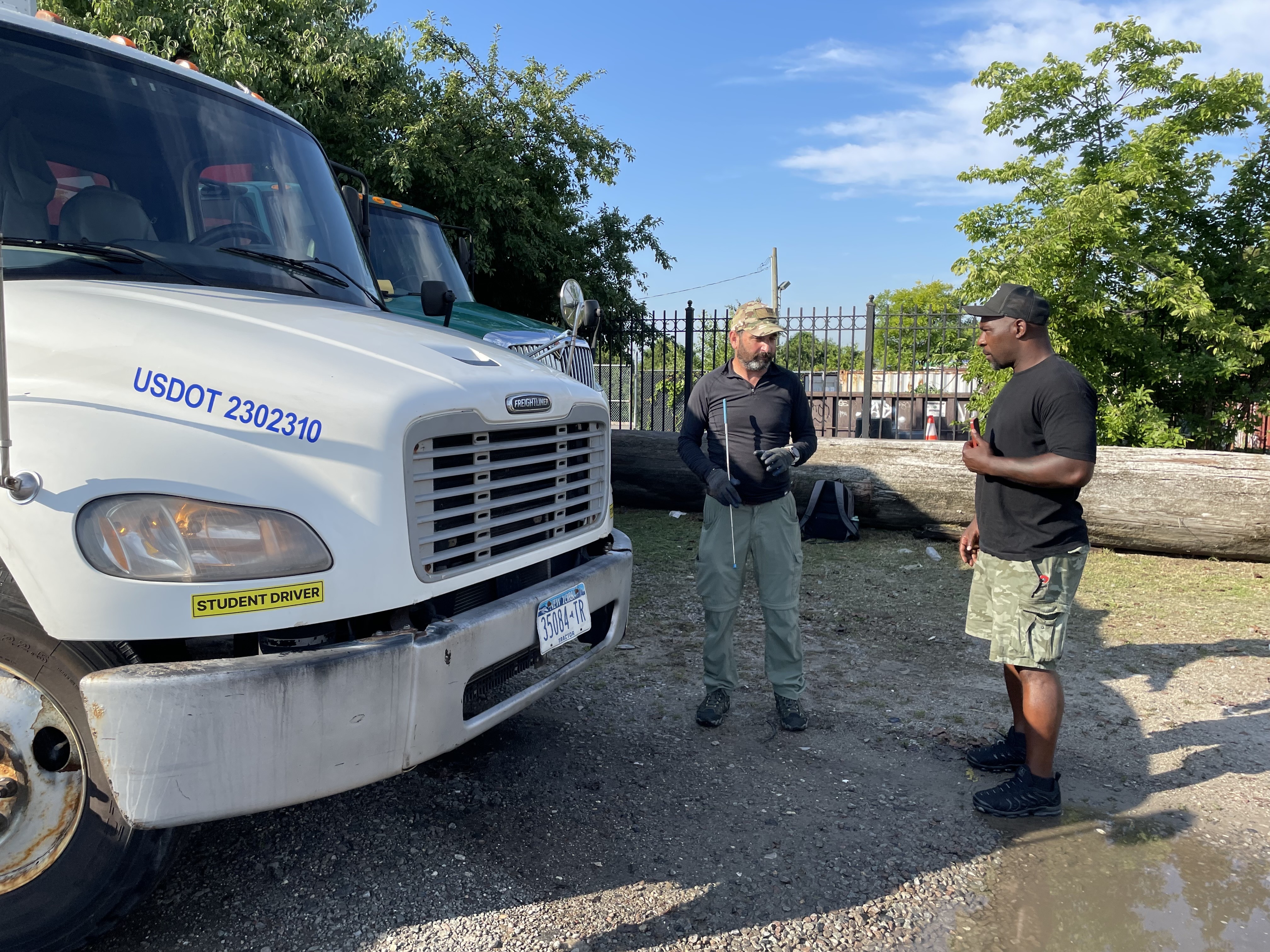 Two men stand next to a white semitruck on a bright summer day.