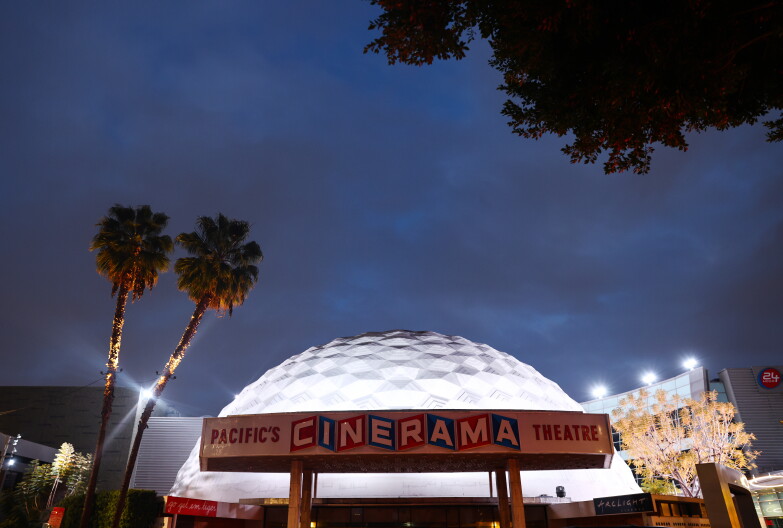 A white domed building is lit up against a night sky. In front of the building is a sign that reads, "Pacific's Cinerama Theatre."