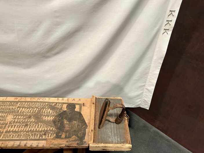 A wood plank shows an image of a person and a drawing of people lined up side by side. A flat iron rests on the plank.