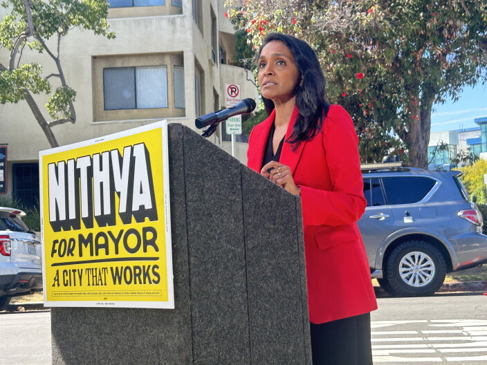 Woman in red blazer at podium.